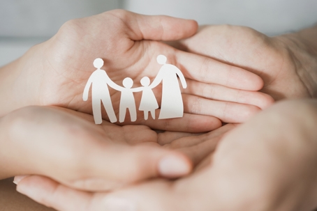 parent and child's hands cupped to hold a paper cutout of a family